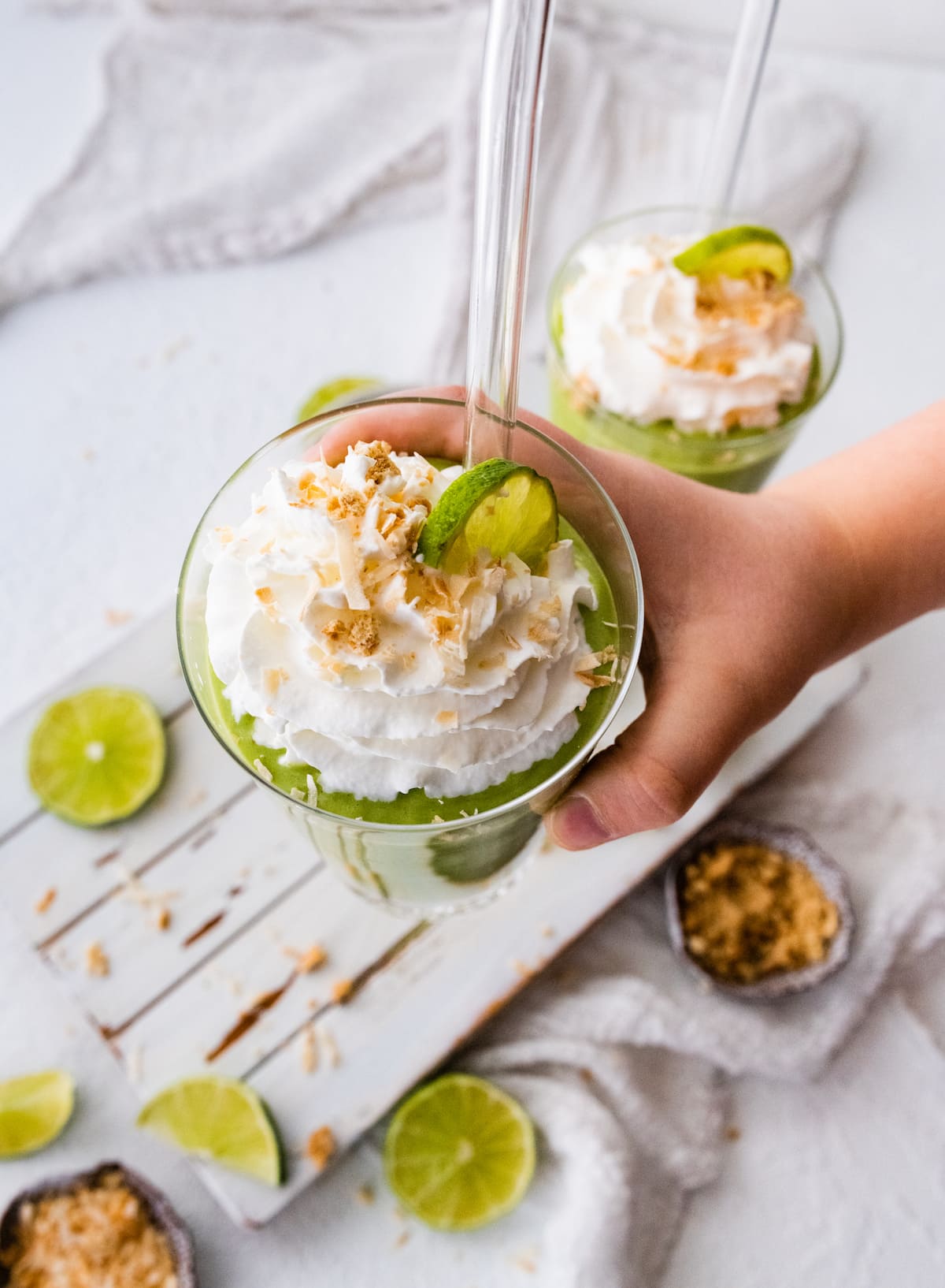 Woman's hand holding a key lime pie smoothie, topped with whip cream, toasted coconut and fresh lime slices.