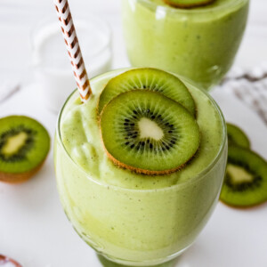 Two kiwi smoothies with straws, topped with kiwi slices.