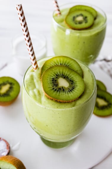 Two kiwi smoothies with straws, topped with kiwi slices.