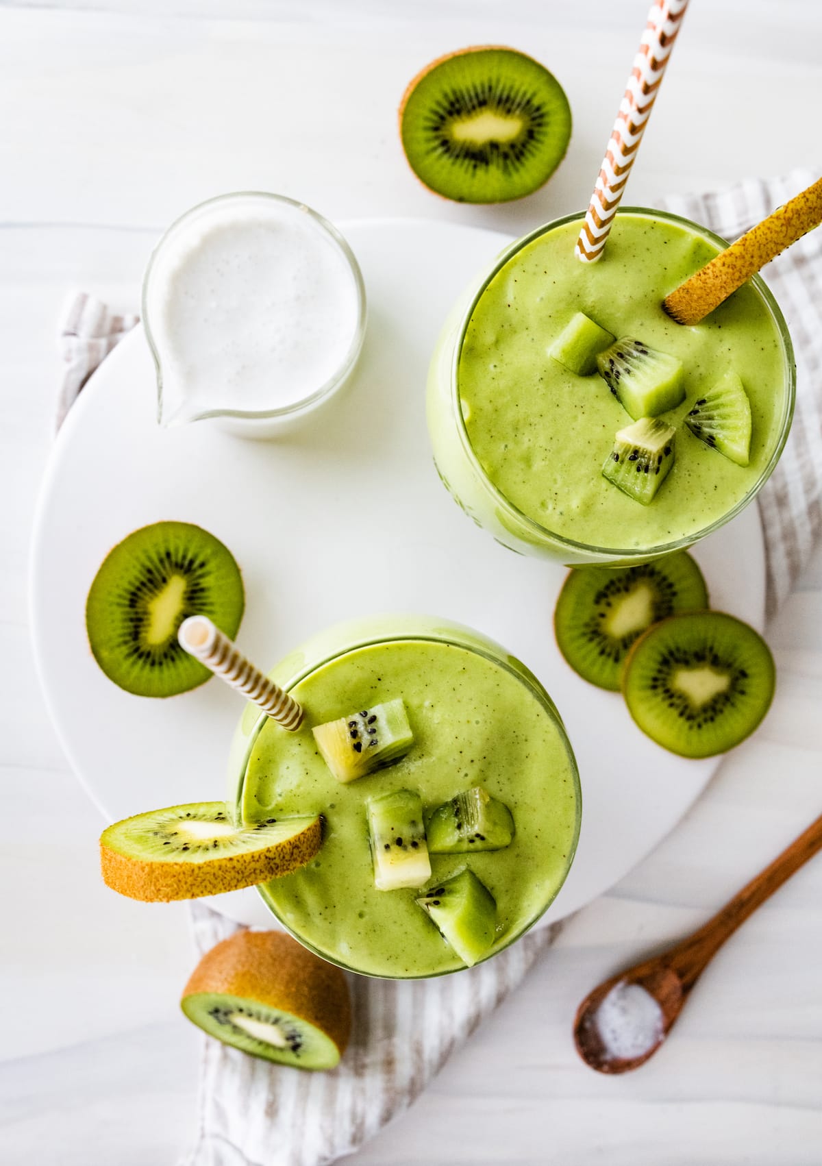 Two kiwi smoothies with straws, topped with kiwi chunks.