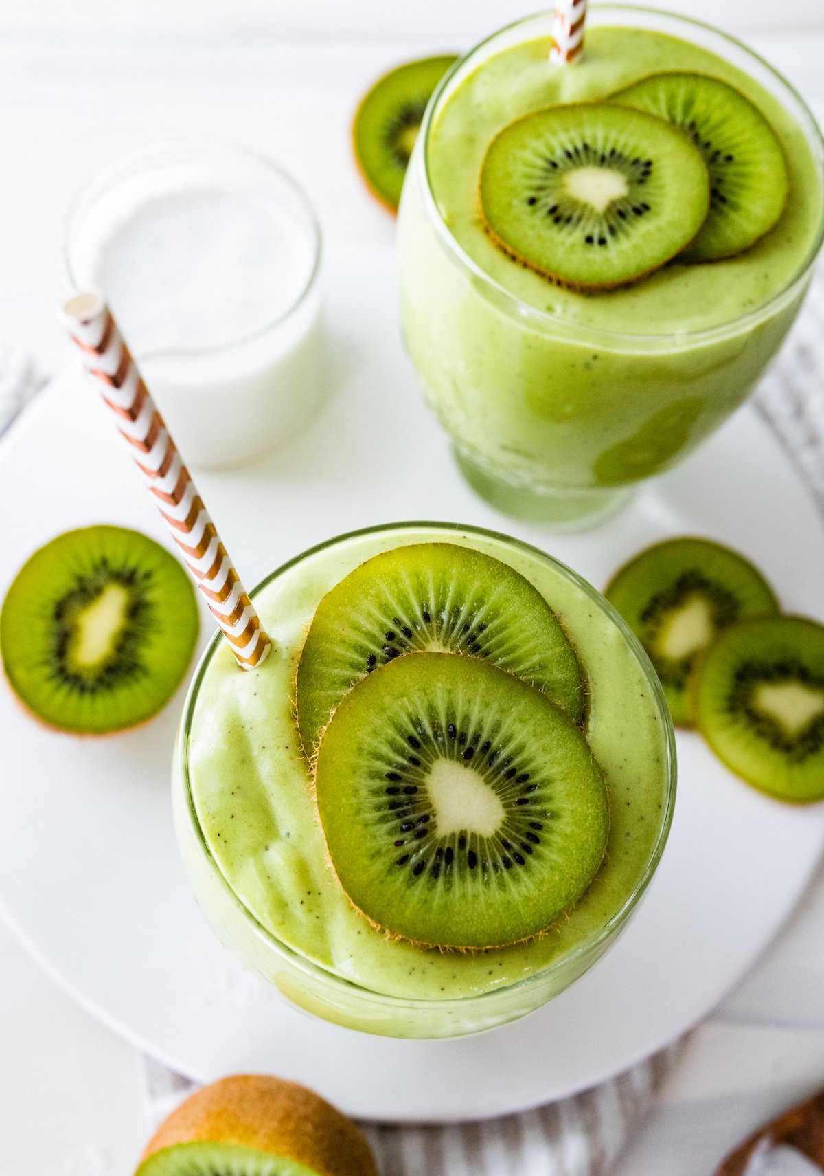 Two kiwi smoothies with straws, topped with kiwi slices.