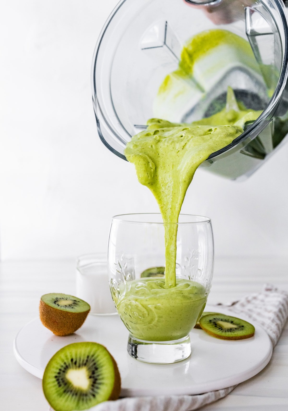 Woman's hand pouring kiwi smoothie in glass.