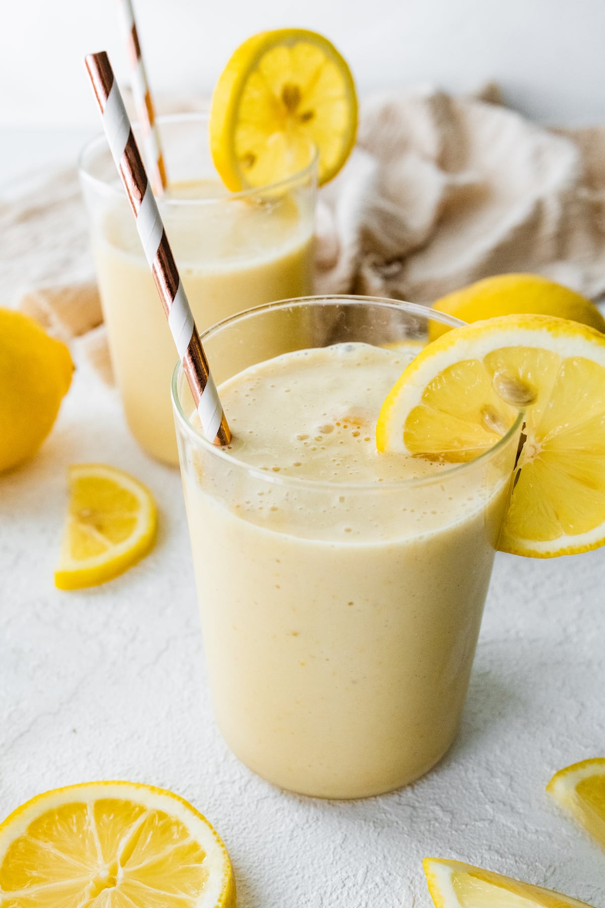 Two lemon smoothies with straws and fresh lemon slices.