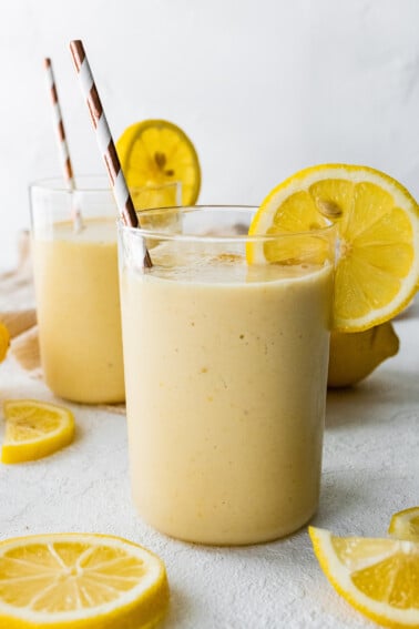 Two lemon smoothies with straws and fresh lemon slices.