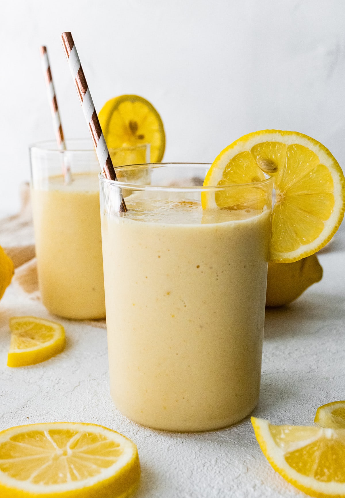 Two lemon smoothies with straws and fresh lemon slices.