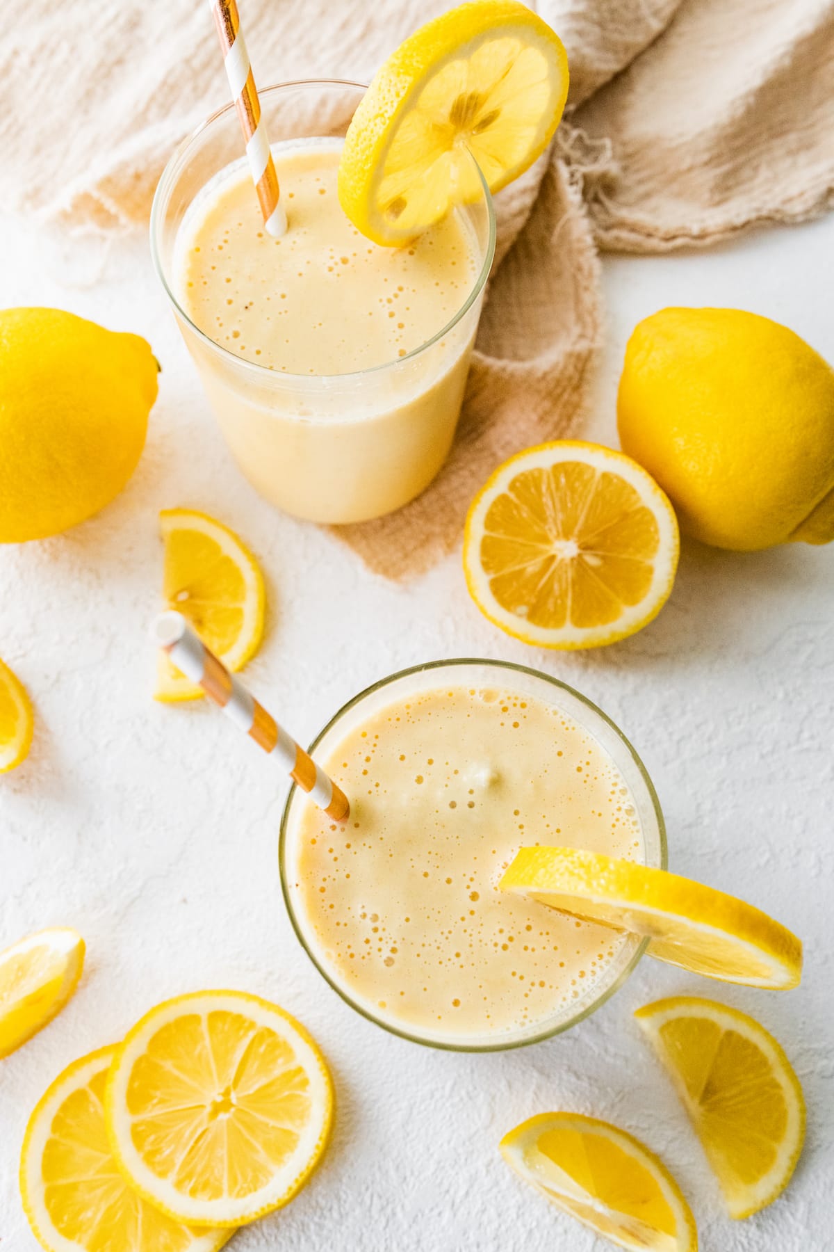 Overhead view of two lemon smoothies with straws and fresh lemon slices.