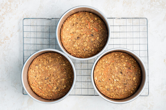 3 6" oatmeal carrot cakes cooling in the pans sitting on a wire rack.