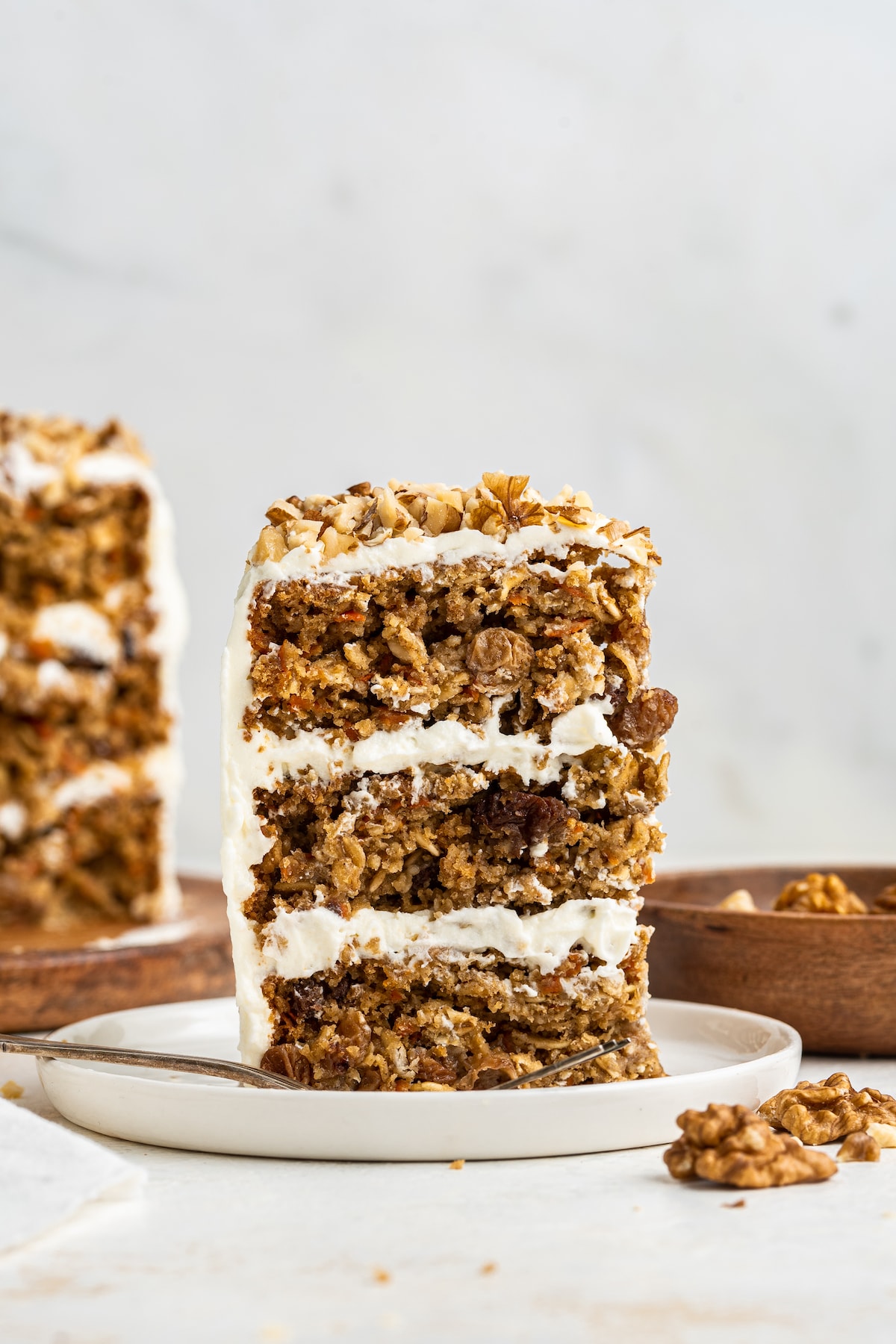 A slice of a 3-layer oatmeal carrot cake standing up vertical on a white plate.