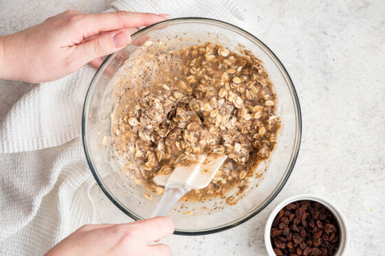Woman's hands mixing oatmeal raisin protein bars in glass mixing bowl.