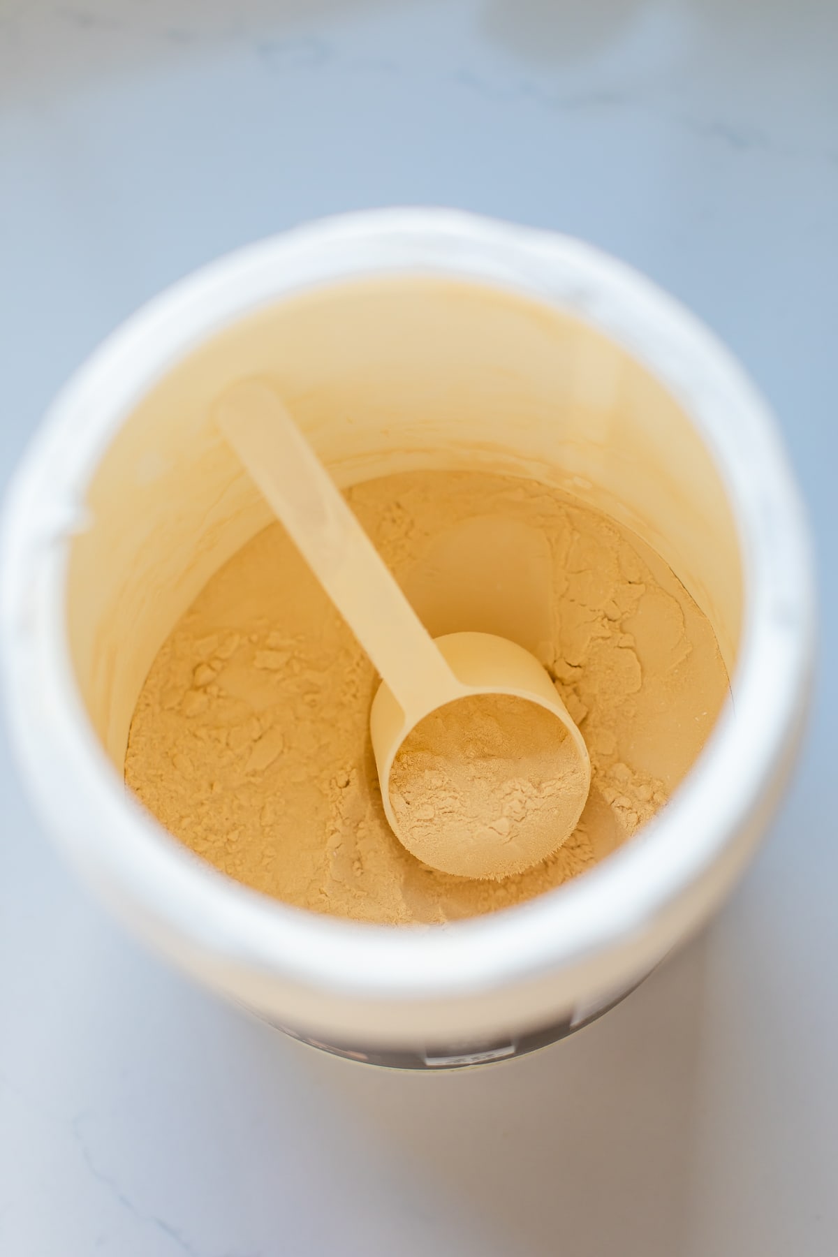 Inside Nuzest vanilla protein powder container with scoop.