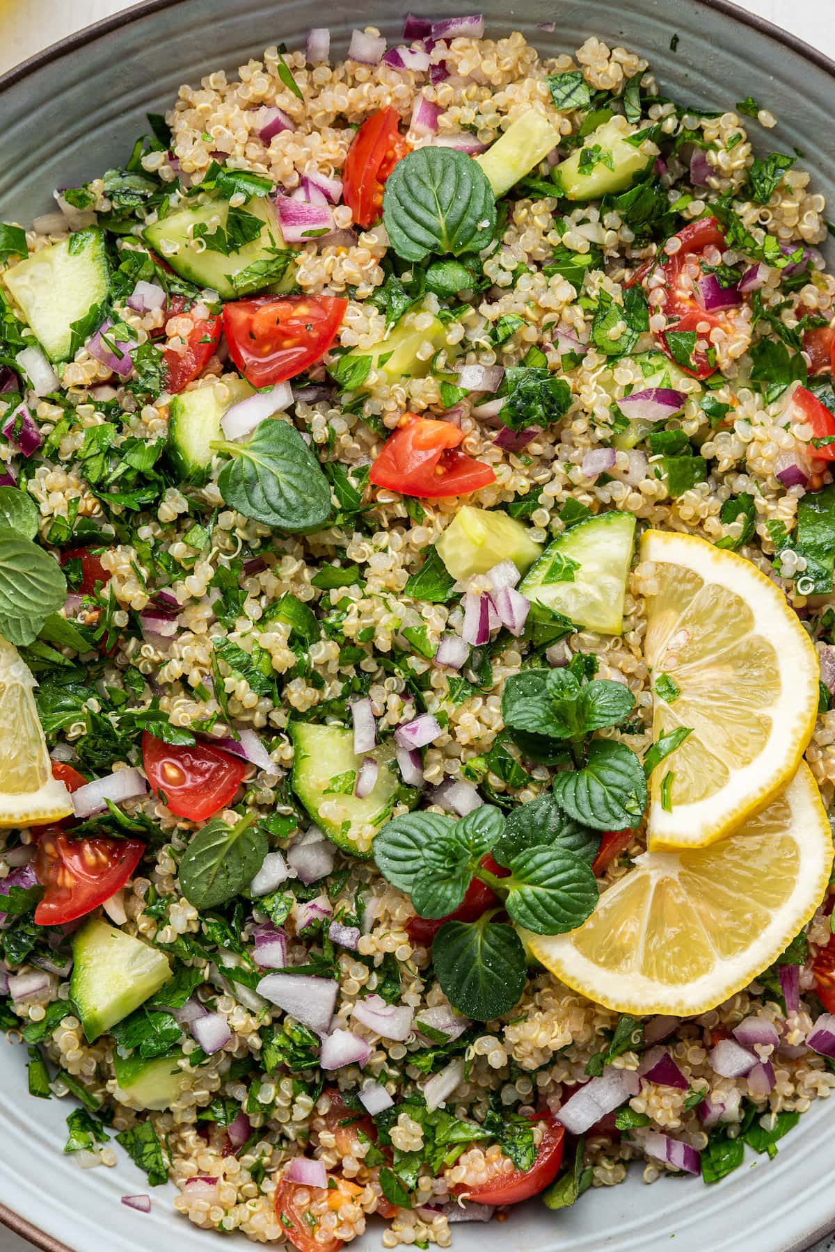 Close up photo of a quinoa tabbouleh salad topped with fresh lemon slices and fresh herbs.