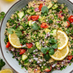 Quinoa tabbouleh in a serving bowl topped with fresh lemon slices and fresh herbs.