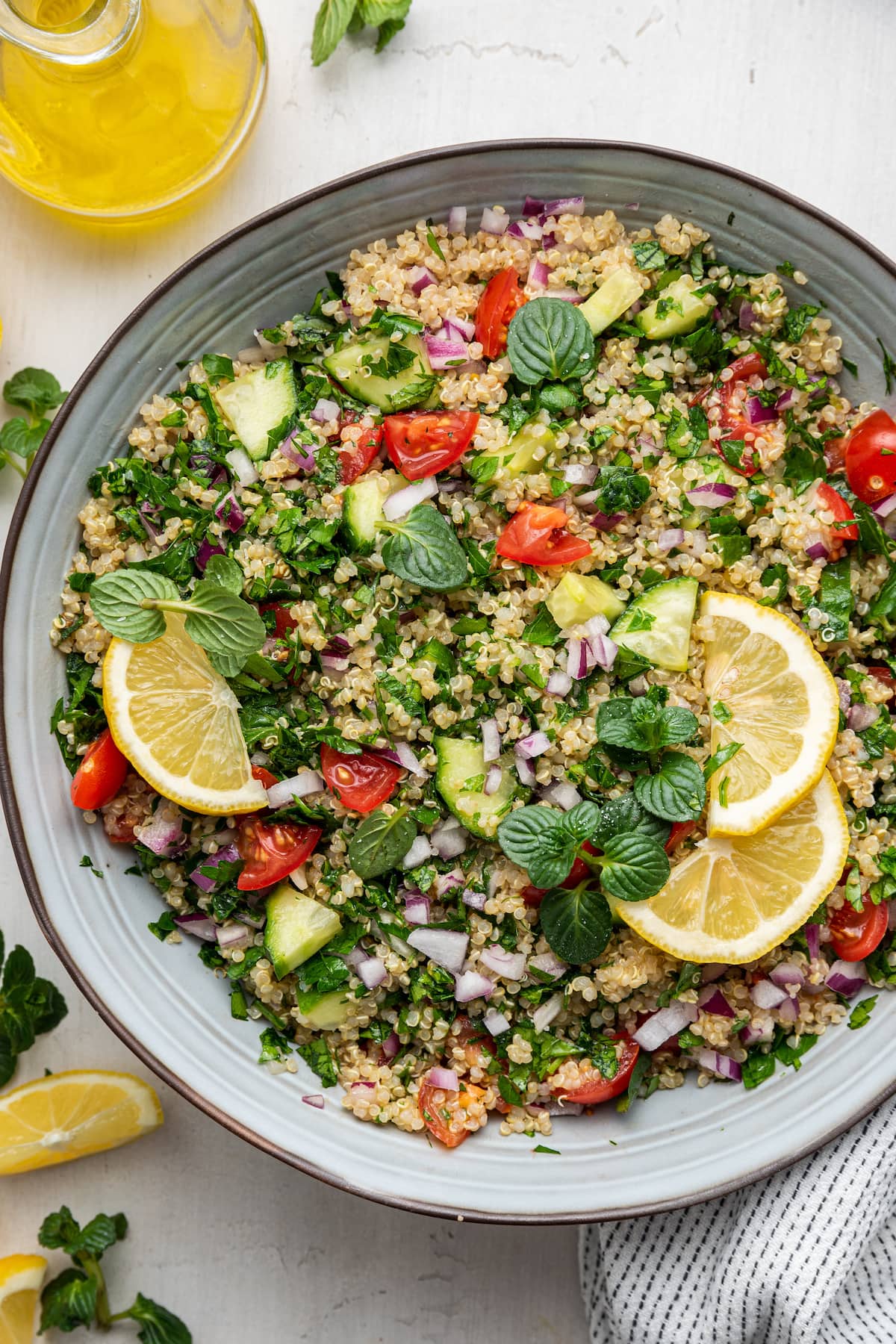 Quinoa tabbouleh in a serving bowl topped with fresh lemon slices and fresh herbs.