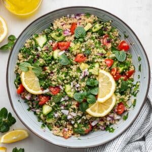 Quinoa tabbouleh in a serving bowl topped with fresh lemon slices and fresh herbs.