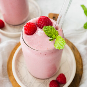 Raspberry smoothie with straw, topped with fresh raspberries and fresh mint.