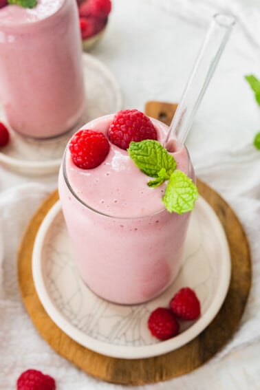 Raspberry smoothie with straw, topped with fresh raspberries and fresh mint.