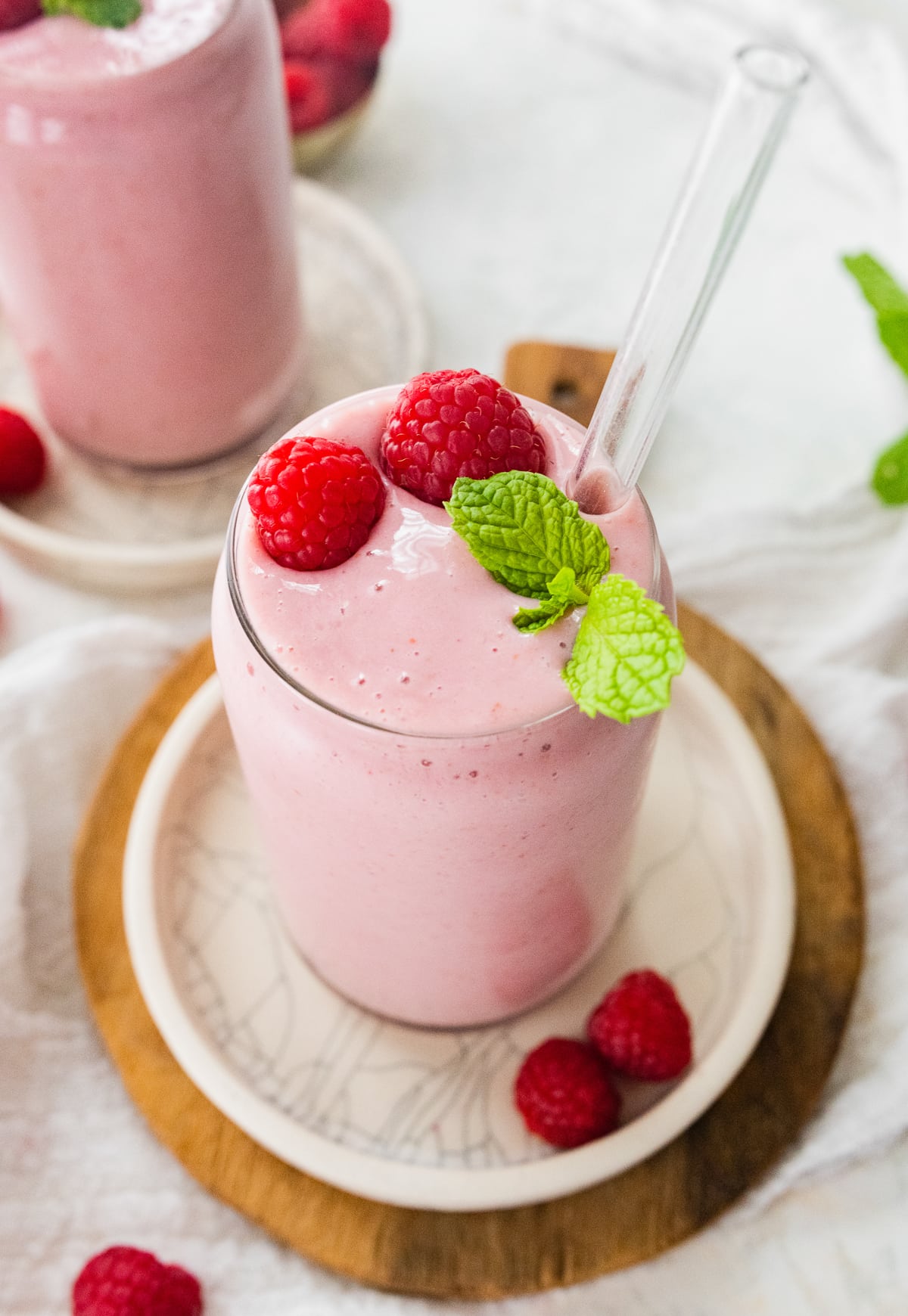 Raspberry smoothie with straw, topped with fresh raspberries and fresh mint.