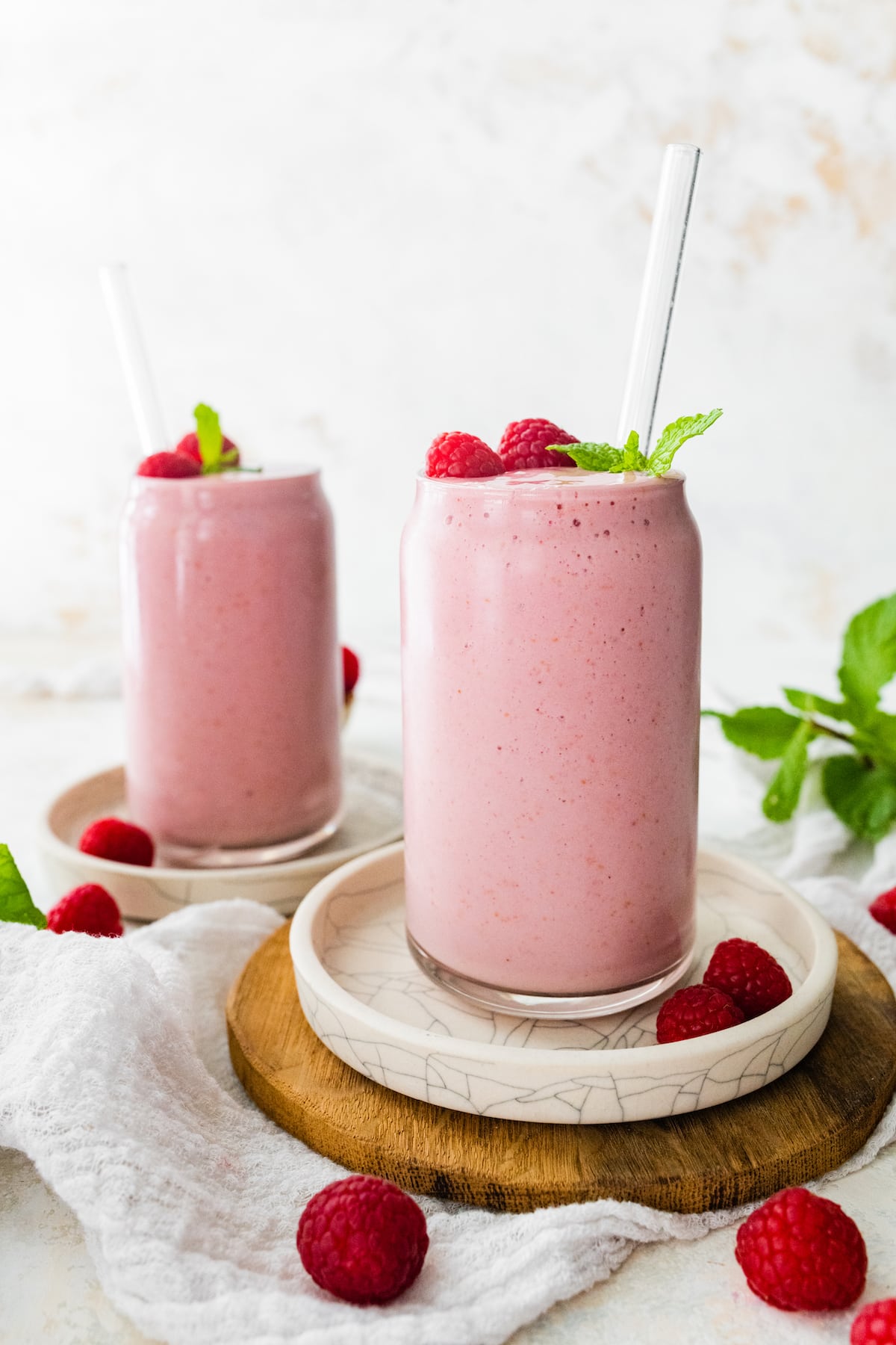 Two raspberry smoothies in glasses with straws.