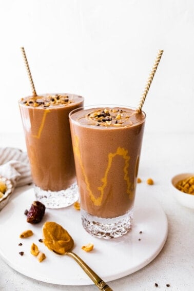 Straight shot of two snickers protein smoothies with drizzle of peanut butter inside glasses.