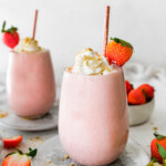 Two strawberry cheesecake smoothies topped with whipped cream and a fresh strawberry.