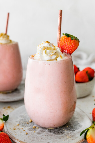 Two strawberry cheesecake smoothies topped with whipped cream and a fresh strawberry.