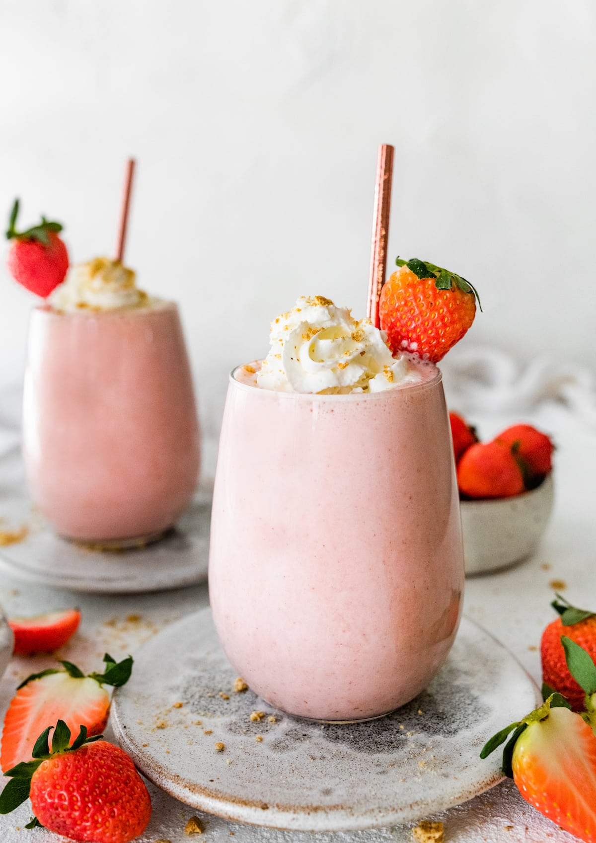 Two strawberry cheesecake smoothies topped with whipped cream and a fresh strawberry.