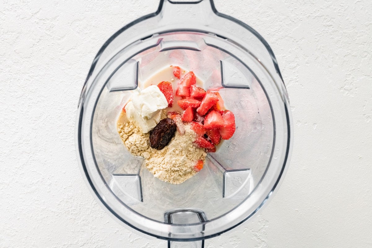 Ingredients for a strawberry cheesecake smoothie in blender.