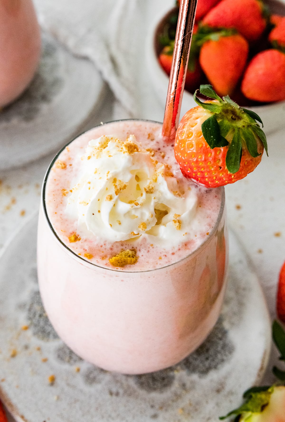 A strawberry cheesecake smoothie in a glass topped with whipped cream and crushed graham crackers.
