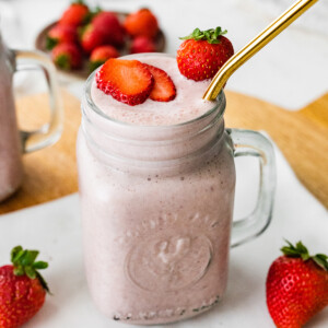 A strawberry protein shake served with a straw and extra strawberries.