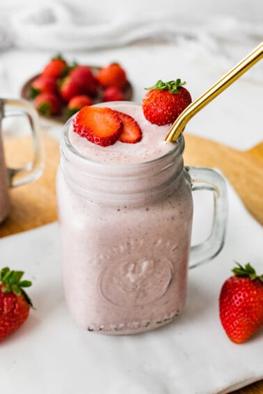 A strawberry protein shake served with a straw and extra strawberries.