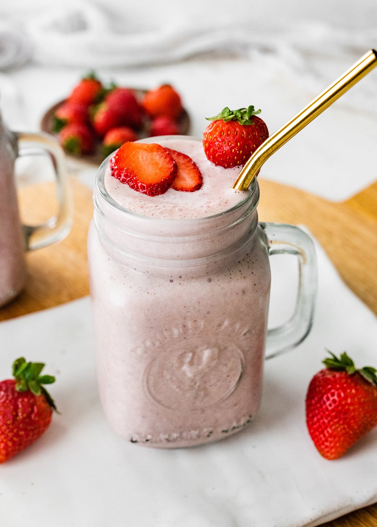 A strawberry protein shake served with a straw and extra strawberries.