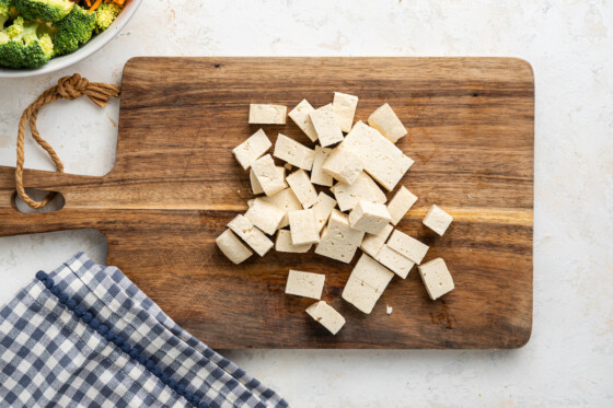 Tofu chopped into chunks on wooden cutting board.