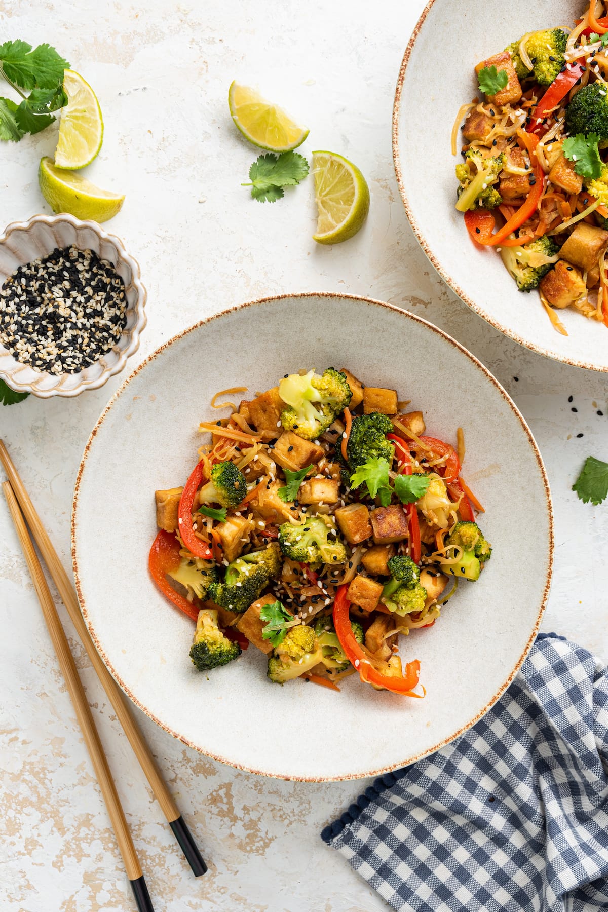 Two tofu cabbage noodle bowls with chopsticks next to one bowl and fresh lime wedges scatted around bowls.