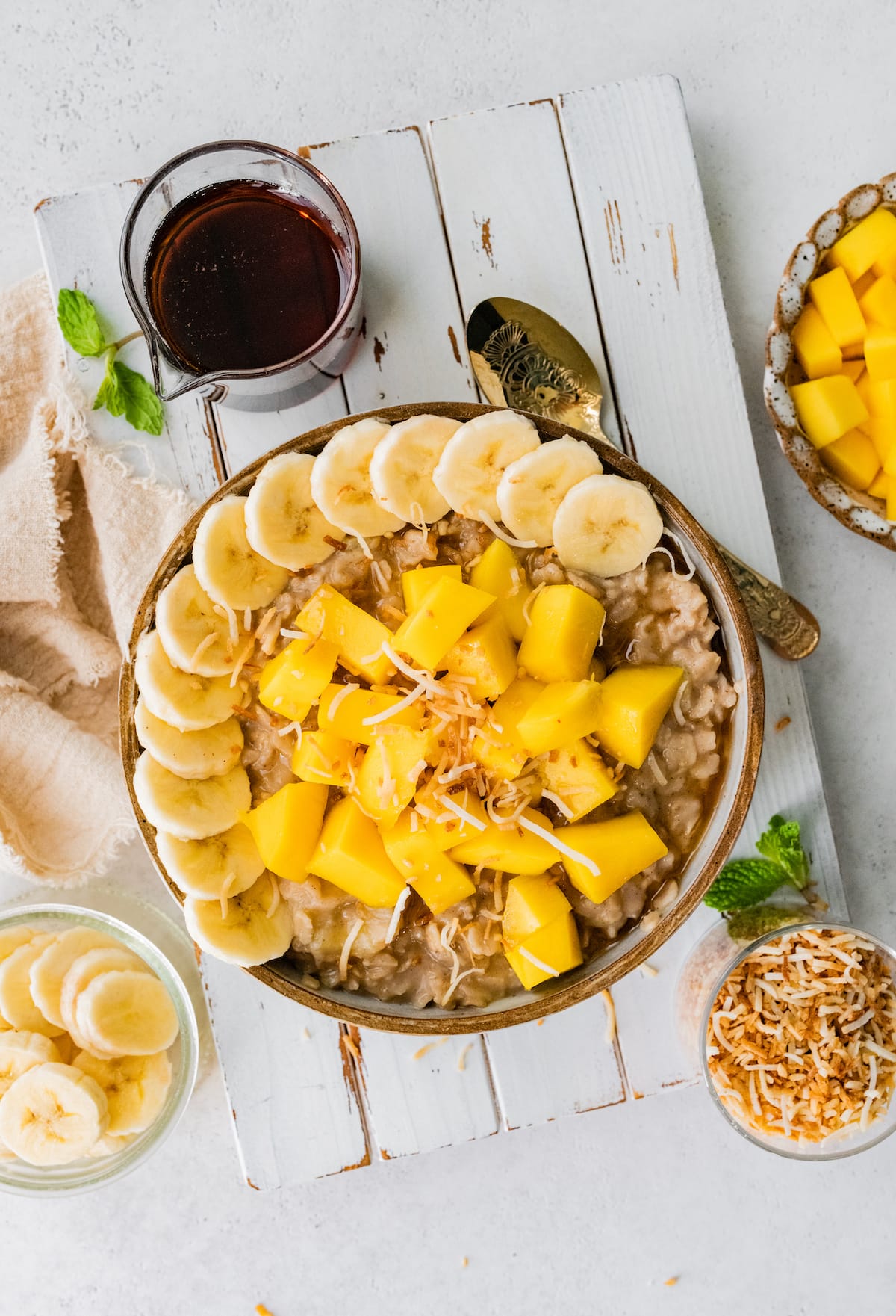 Far away bowl of oatmeal topped with fresh mango, banana slices and toasted coconut.