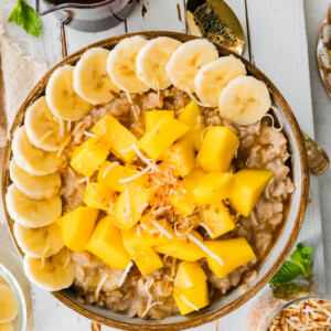 Bowl of oatmeal topped with fresh mango, banana slices and toasted coconut.