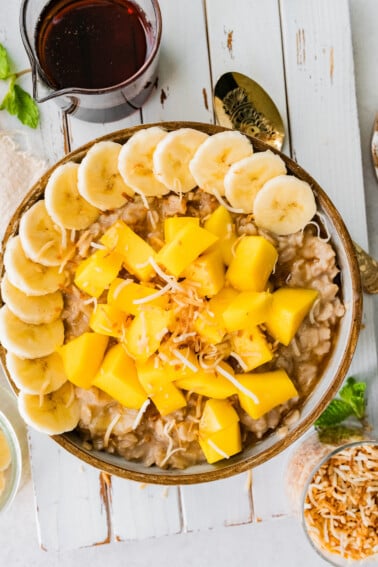 Bowl of oatmeal topped with fresh mango, banana slices and toasted coconut.