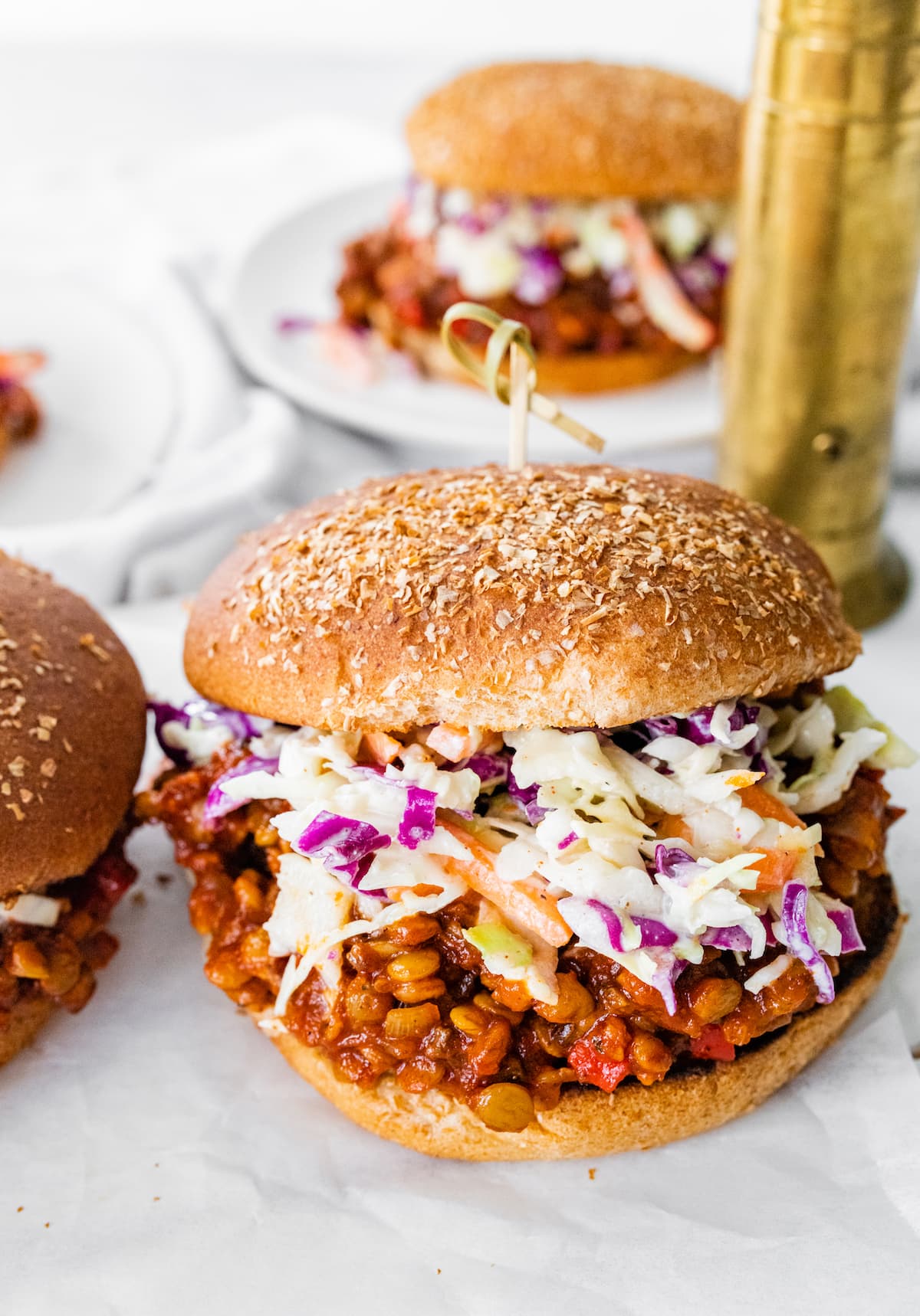 One vegan Sloppy Joe on a whole wheat bun topped with coleslaw with a second vegan Sloppy Joe in the background on a plate.
