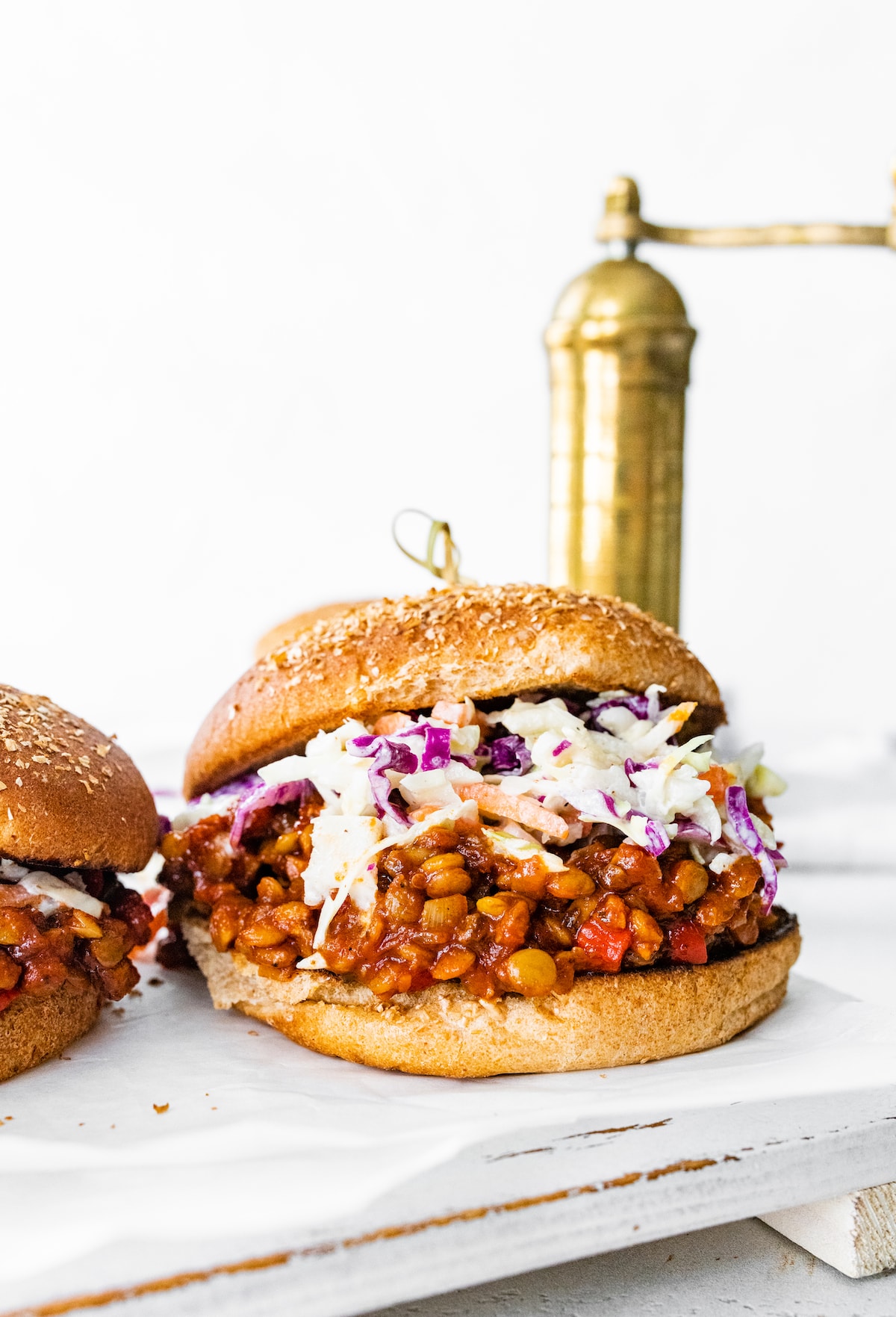 One vegan Sloppy Joe on a whole wheat bun topped with coleslaw with a gold pepper grinder are in the background.