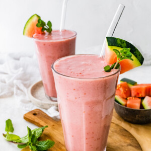 Two watermelon smoothies with straws and fresh watermelon slices.