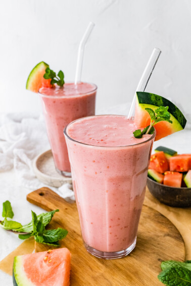 Two watermelon smoothies with straws and fresh watermelon slices.
