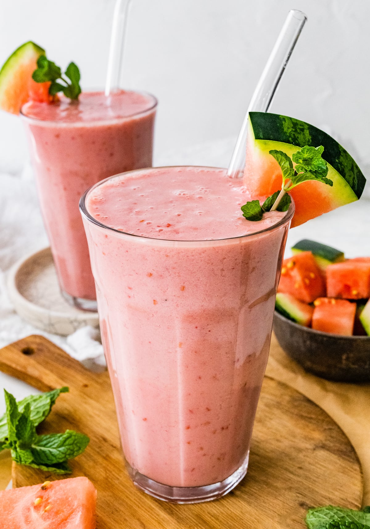 Two watermelon smoothies with straws and fresh watermelon slices.