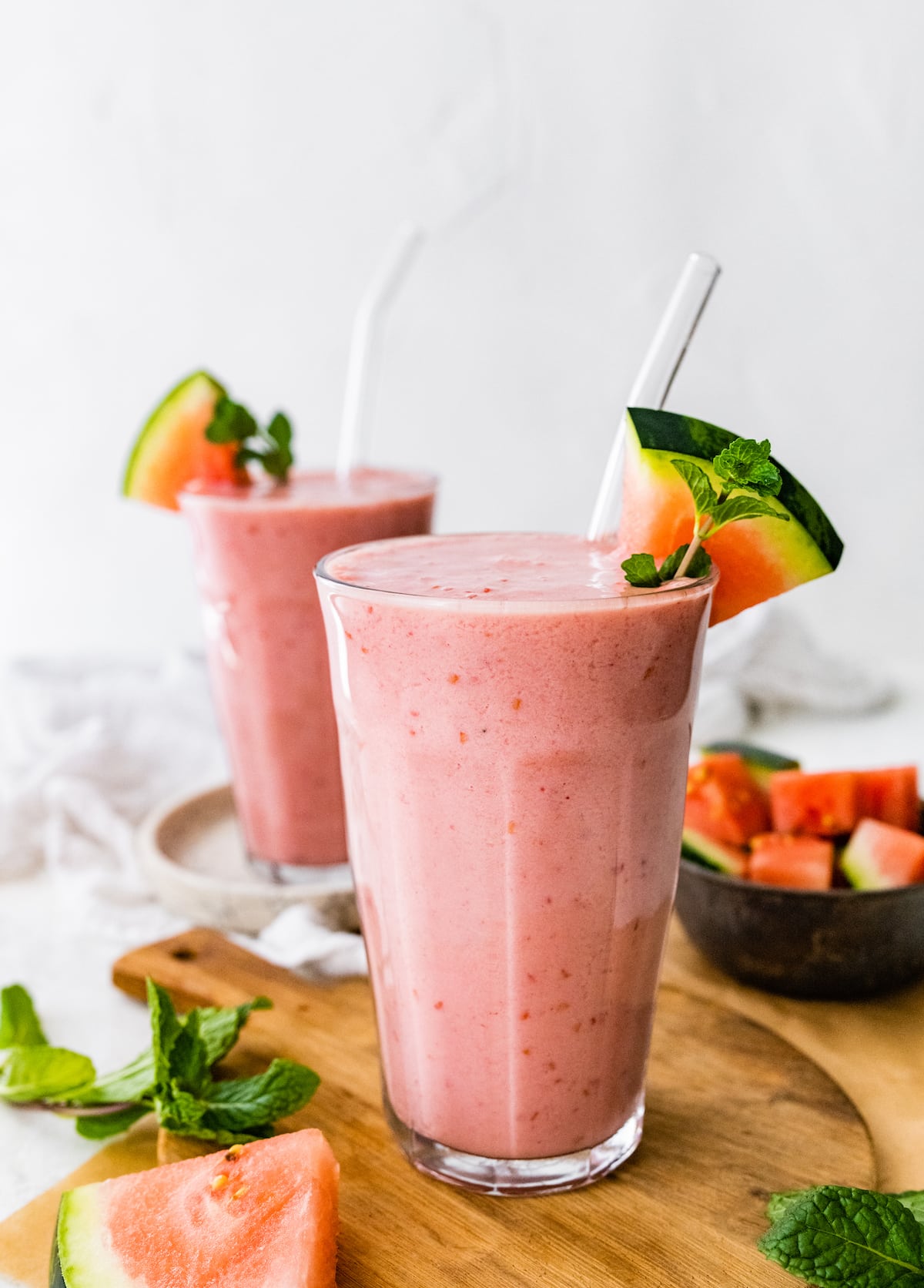 Two watermelon smoothies with straws and slices of fresh watermelon.