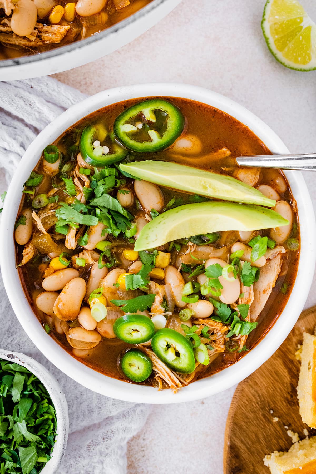 A bowl of white bean chicken chili topped with jalapeño slices and avocado.