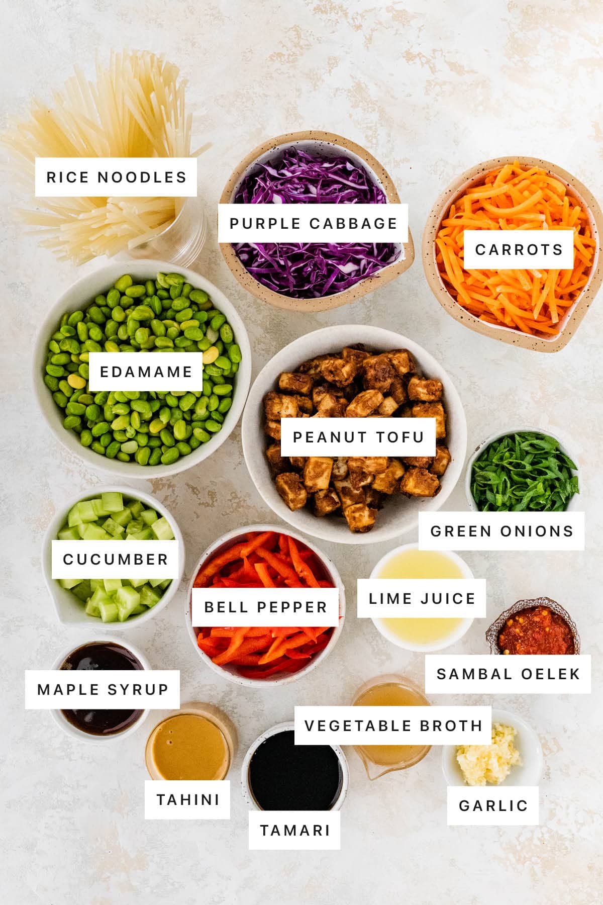 Ingredients measured out to make Asian Noodle Bowl (for Meal Prep): rice noodles, purple cabbage, carrots, edamame, peanut tofu, green onions, cucumber, bell pepper, lime juice, sambal oelek, maple syrup, tahini, tamari, vegetable broth and garlic.