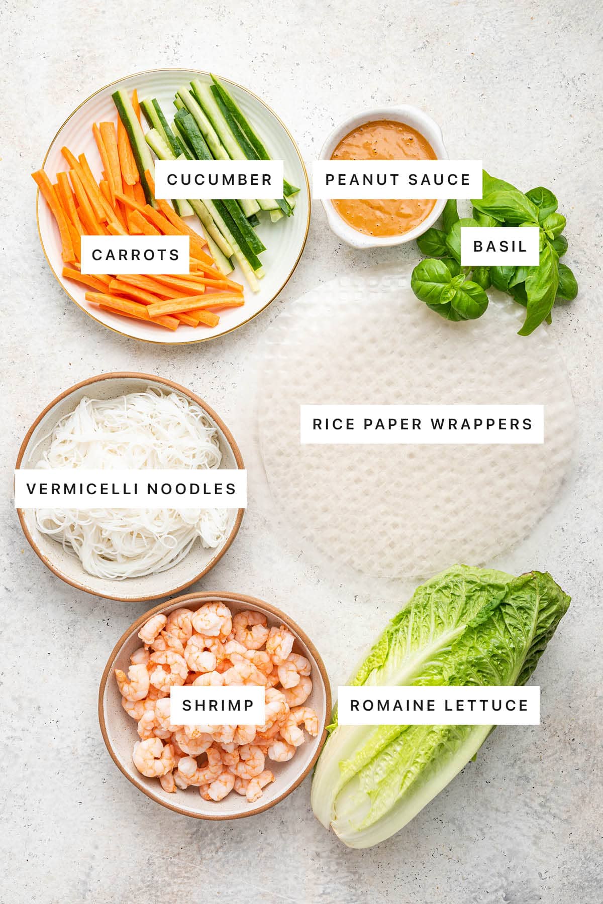Ingredients measured out to make Shrimp Spring Rolls: carrots, cucumber, peanut sauce, basil, rice paper wrappers, vermicelli noodles, shrimp and romaine lettuce.