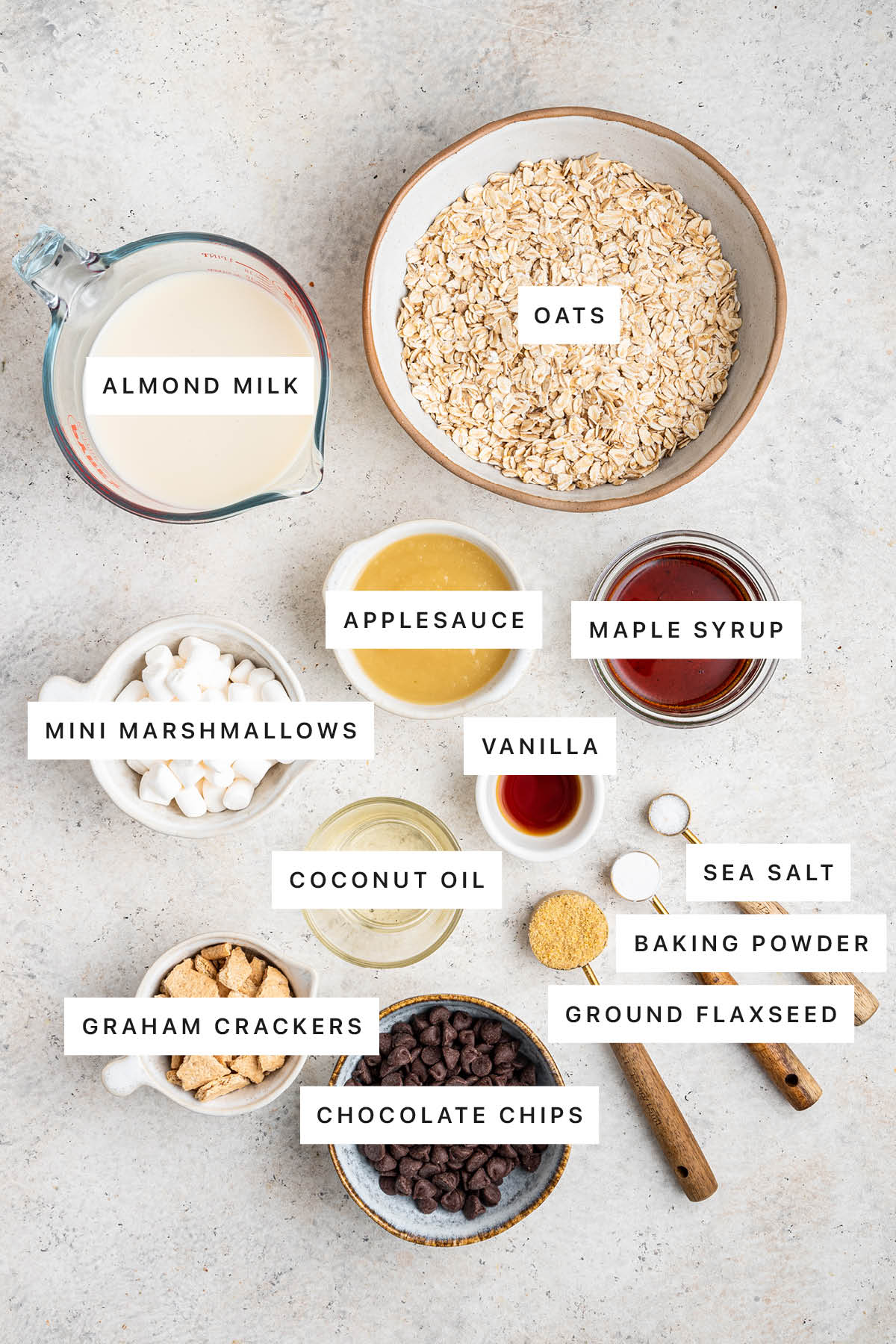 Ingredients measured out to make S'mores Baked Oatmeal: almond milk, oats, applesauce, maple syrup, mini marshmallows, vanilla, coconut oil, sea salt, baking powder, ground flaxseed, graham crackers and chocolate chips.