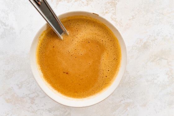 The sauce for the Asian noodle bowl in a white bowl with a metal spoon.