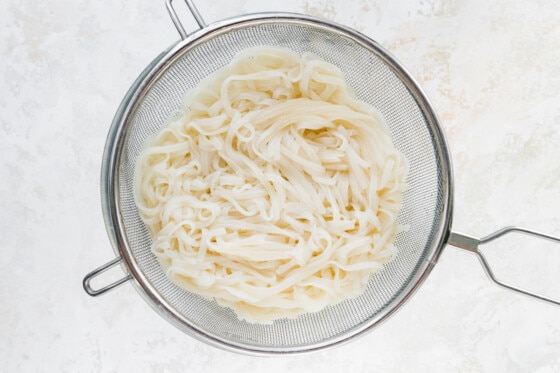 Cooked white rice noodles in a metal strainer.