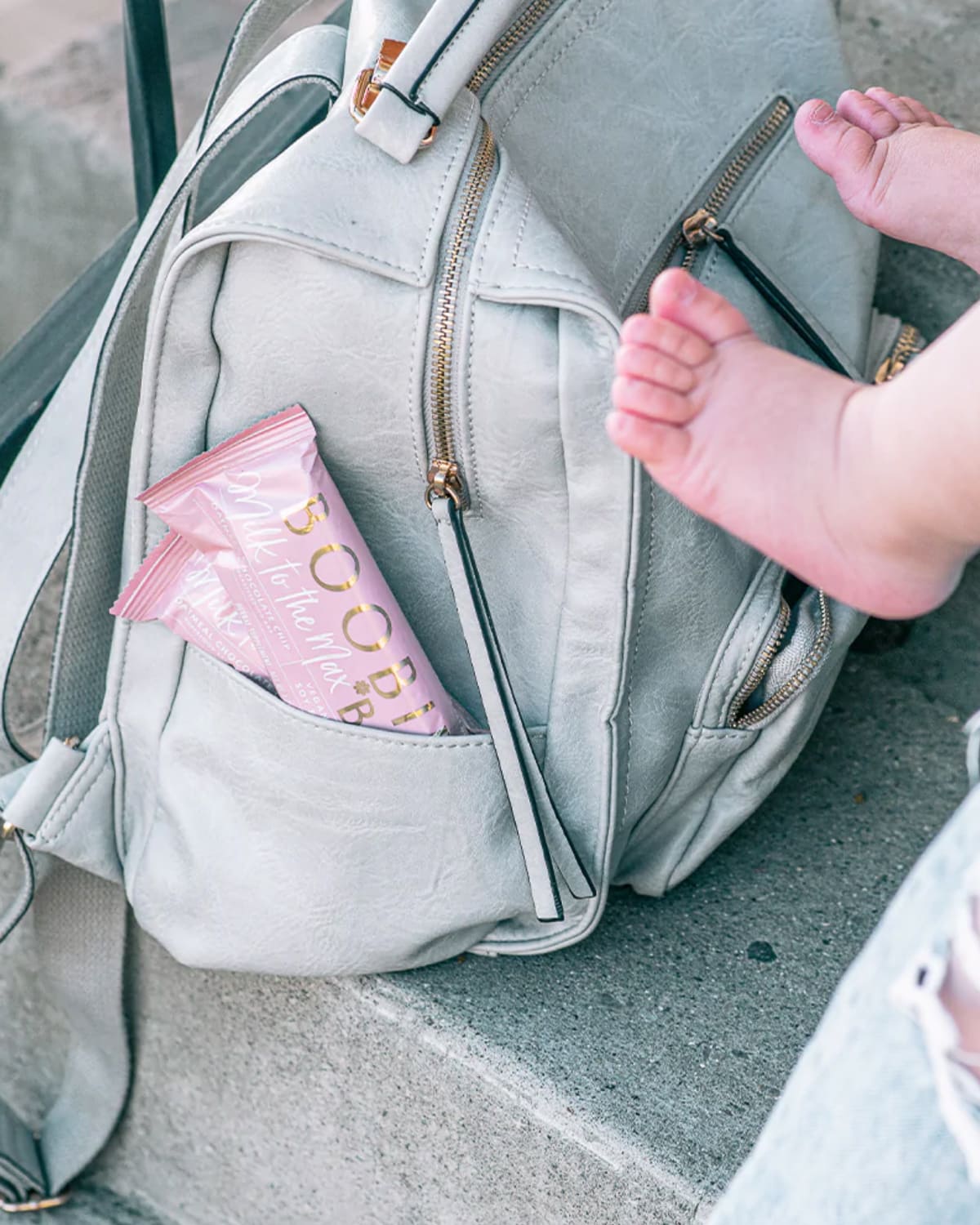 Boobie lactation bars in a gray diaper bag with toddler toes in the frame.