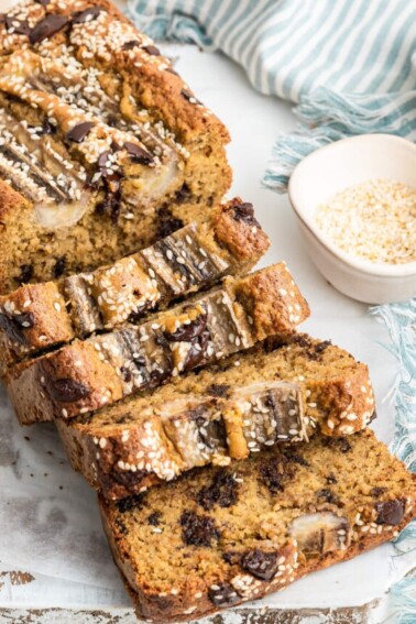 Four slices gently resting on one another in a domino-like formation falling away from the loaf of tahini banana bread.